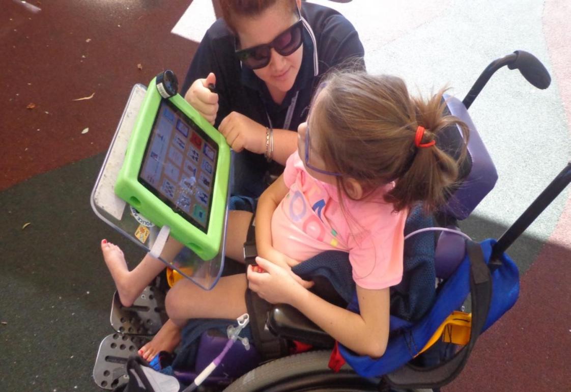 Image description: A young girl who is in a wheelchair is supported by a Student Services Officer (SSO) to use her high-tech POD